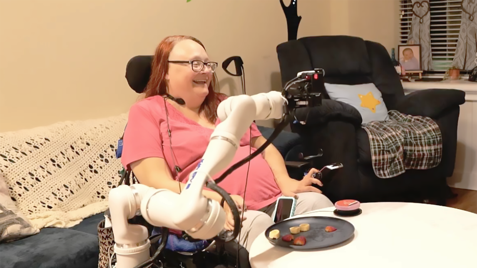 A color photo showing a woman using an assistive robotic device for eating.