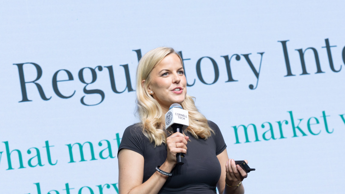 A color photo of a woman speaking with a microphone.