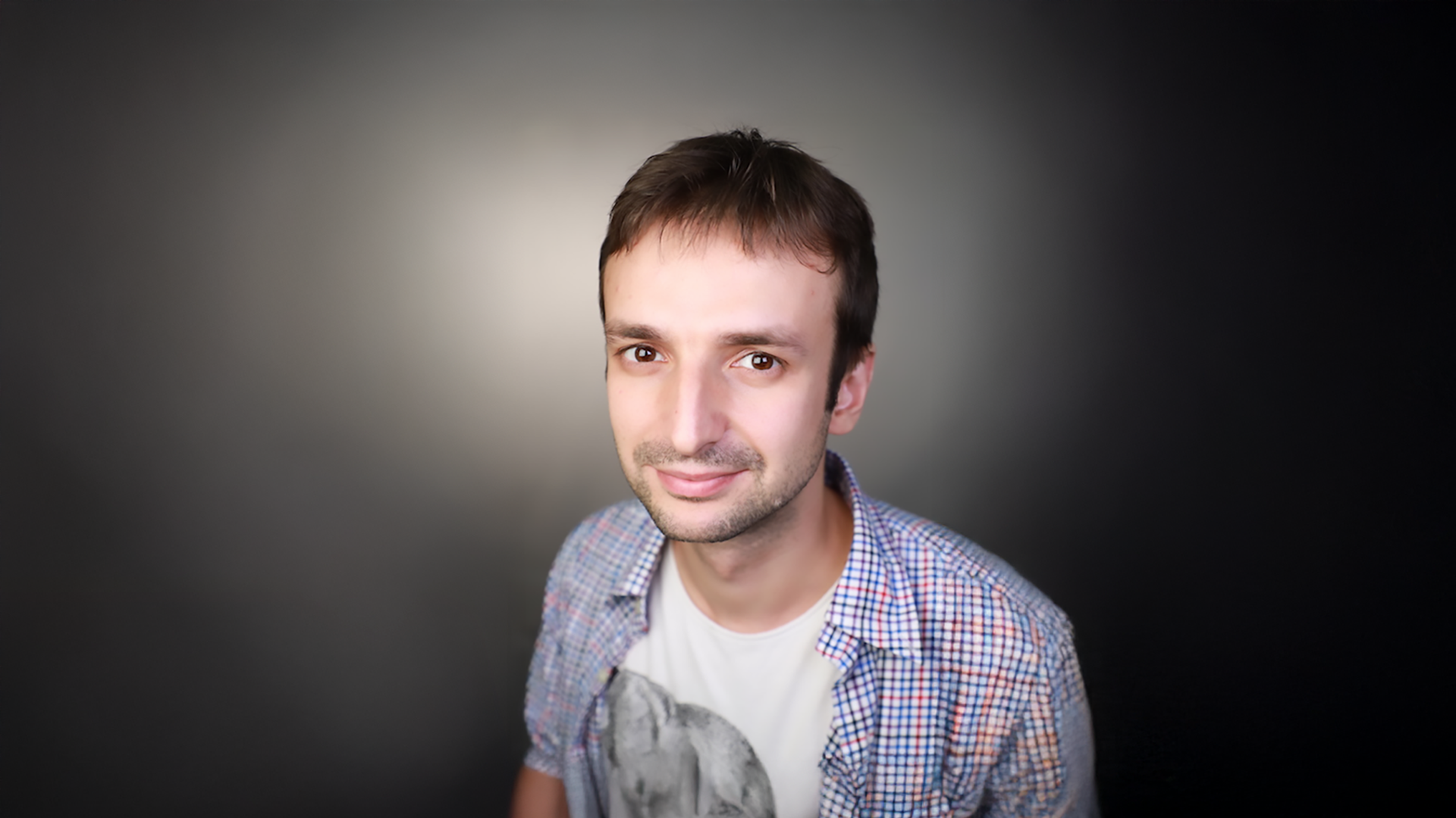 A headshot of a man with short brown hair, wearing a tshirt and button-down