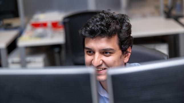 A man with dark hair looks at two computer monitors