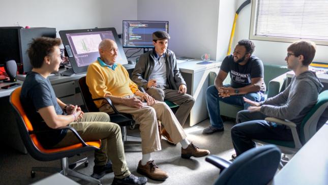 Five men sit around a semi-circle in a computer lab setting.
