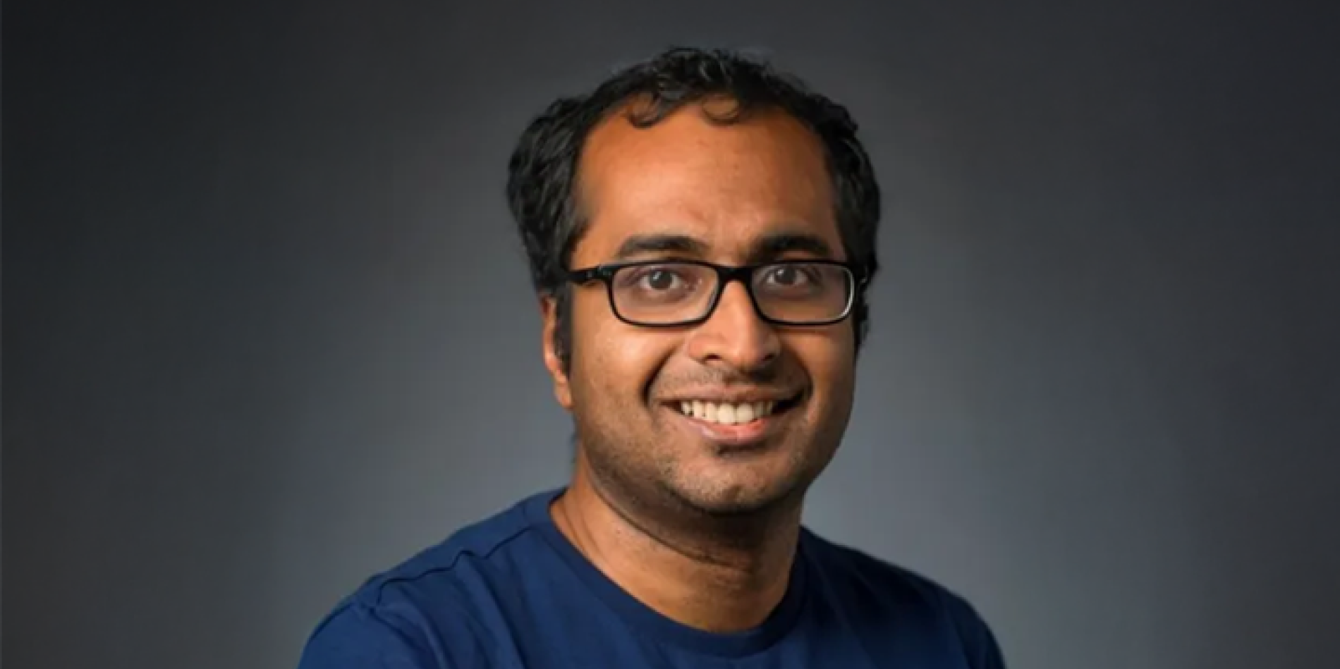 A photo of Bharath Hariharan, a smiling man with short dark hair, glasses and a blue shirt in front of a gray background