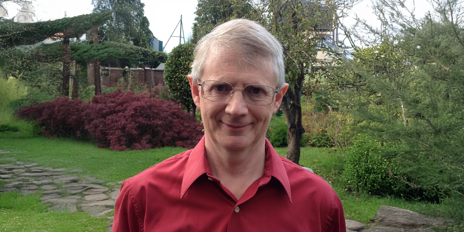 A color photo of a man with glasses standing outside.