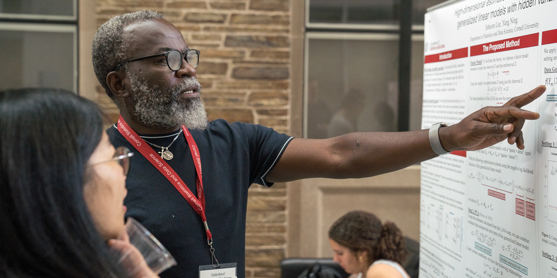 A color photo of a man pointing at a poster while discussing it with a young woman.