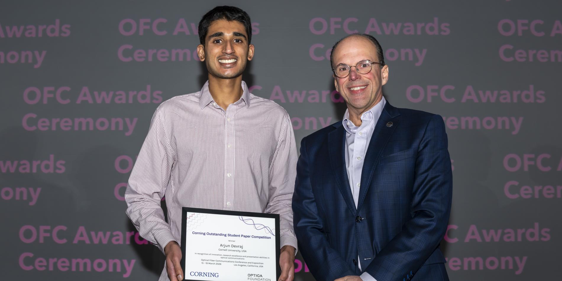 A color photo of two men. One holding a certificate.