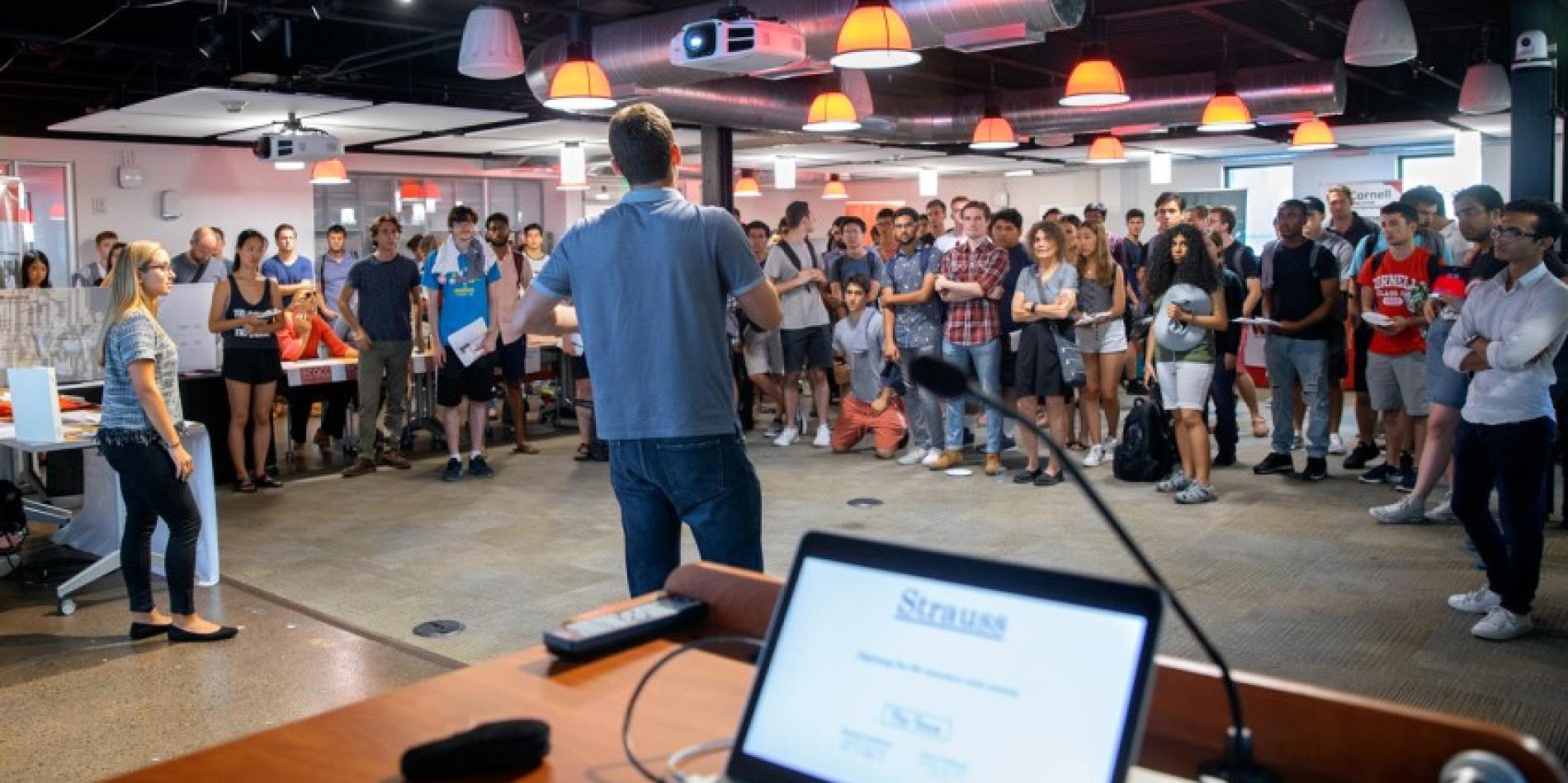 wide view of a room with a crowd of people listening to a man speak in the center