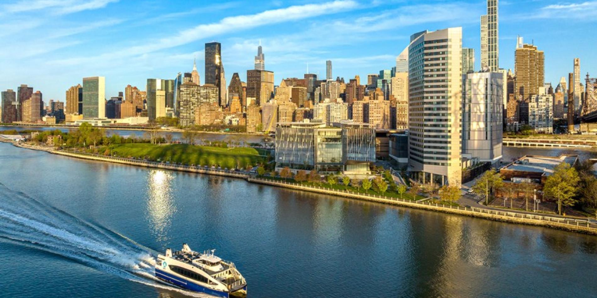 The Cornell Tech campus where it meets the water on a sunny day; a ferry passes through.