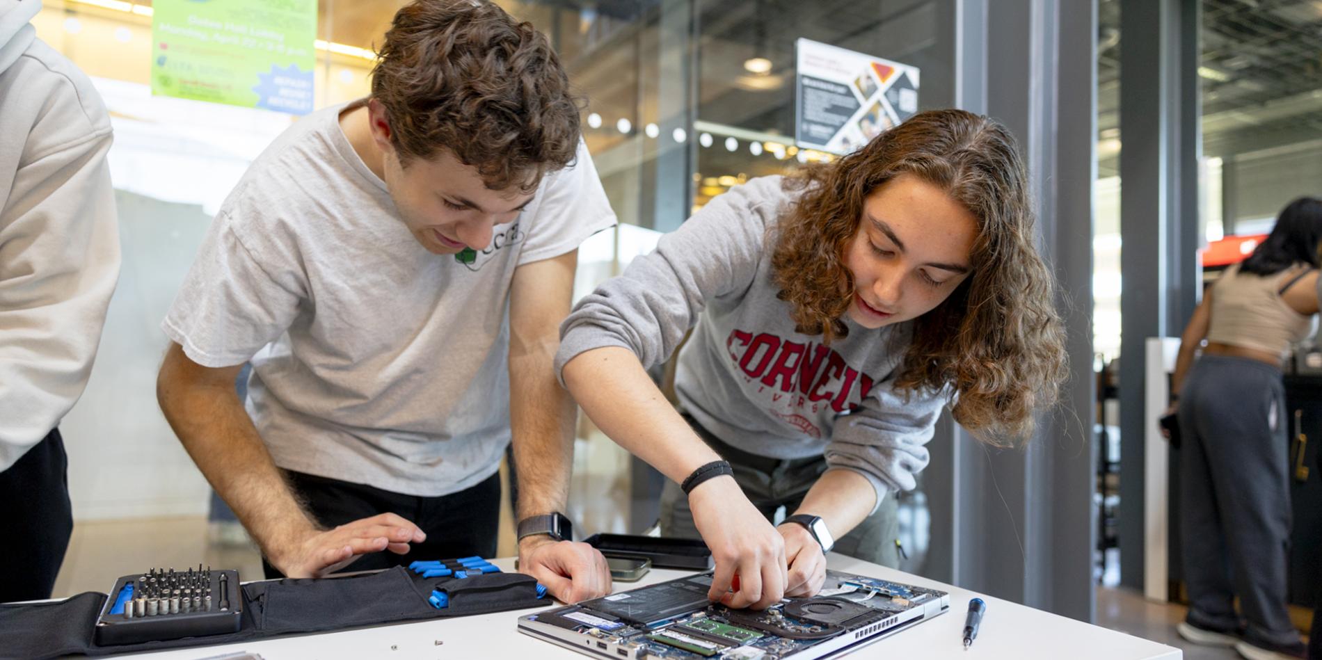 Two students tinker with a laptop.