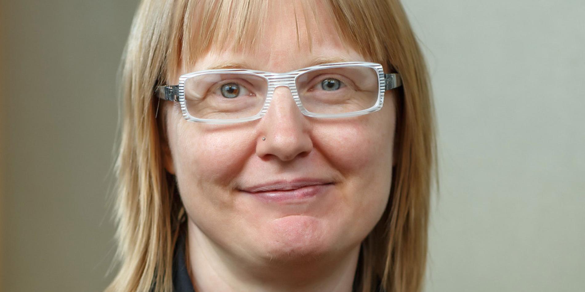 a white woman with short blonde hair and white eyeglasses smiles