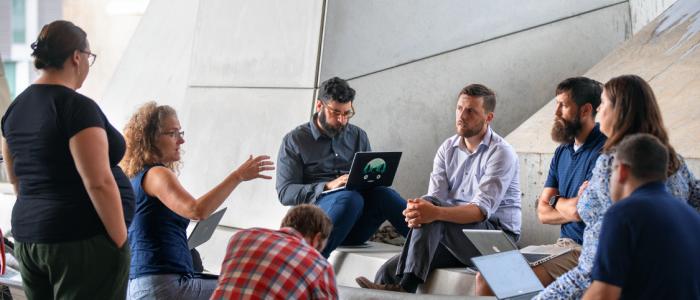 woman in blue shirts talks with a group of people seated around her
