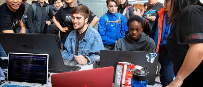 Students gathering around watching people working on computers.