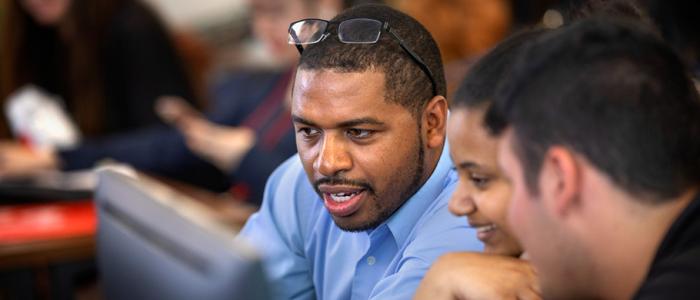 Students collaborate around a computer, focused on their shared work.