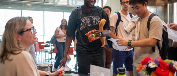 two male students greet a woman with blonde hair and a table 