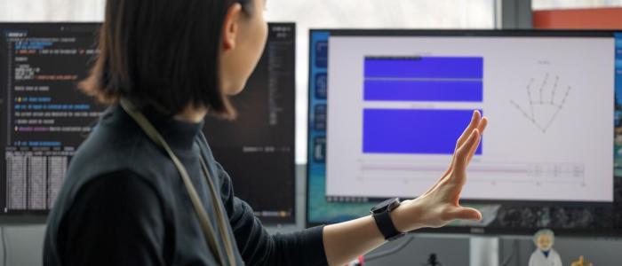 a women with short black hair holds up a hand in front of a computer screen