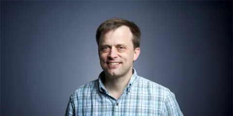 A color photo of Andrew Myers in front of a grey background