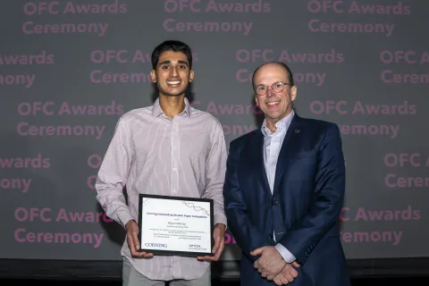 A color photo of two men. One holding a certificate.