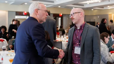 President Kotlikoff shakes the hand of a man with a mustache wearing glasses