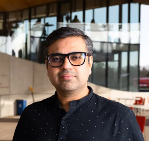 Aditya Vashistha stands and stares at the camera wearing a button-down shirt