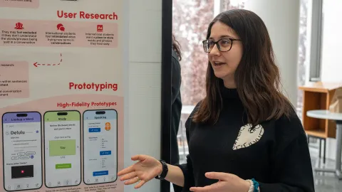 a female student with long brown hair and glasses presents in front of a poster