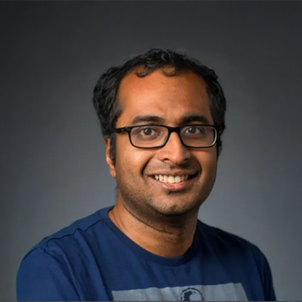 A photo of Bharath Hariharan, a smiling man with short dark hair, glasses and a blue shirt in front of a gray background