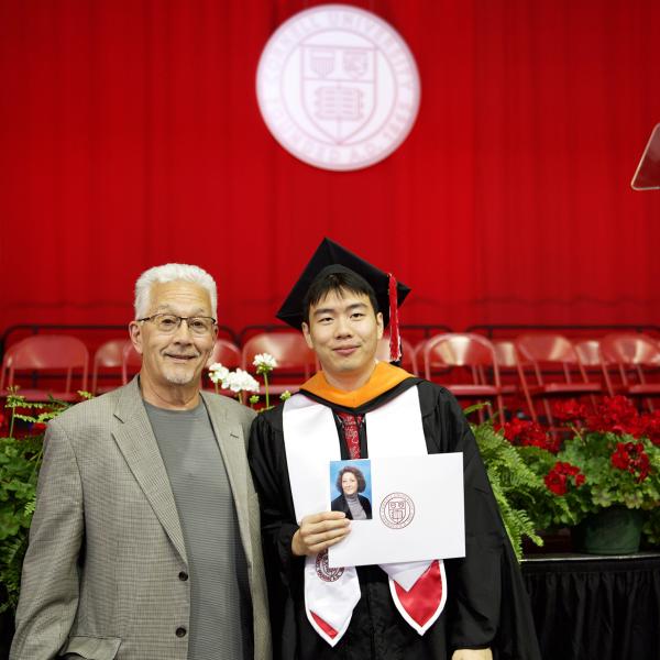 A color photo of a recent graduate in regalia with a family member.