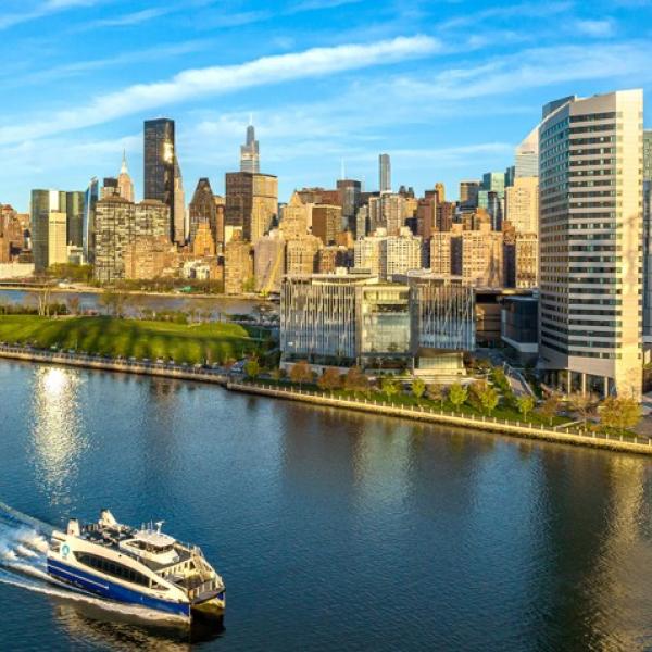 The Cornell Tech campus where it meets the water on a sunny day; a ferry passes through.