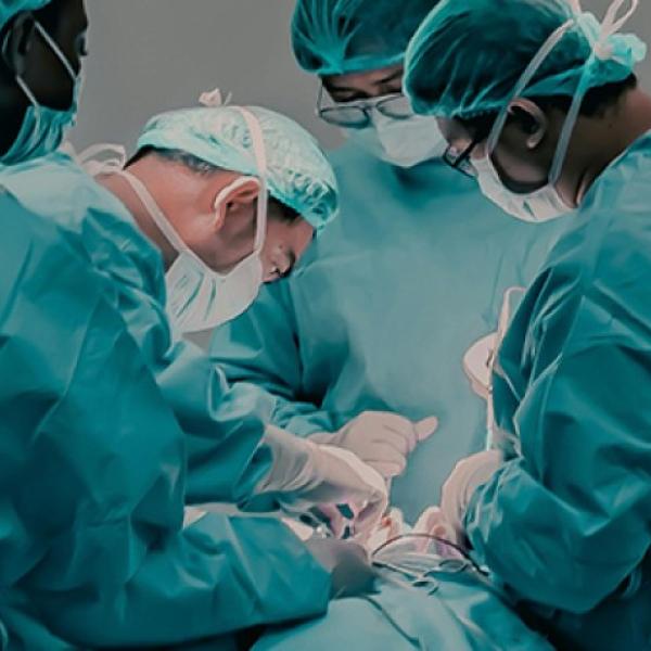 Four healthcare professionals in green gowns perform surgery on a patient.