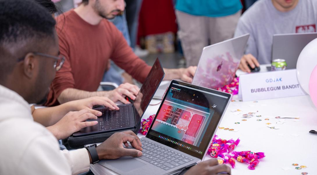 Four men sit at a round table playing videogames on laptops