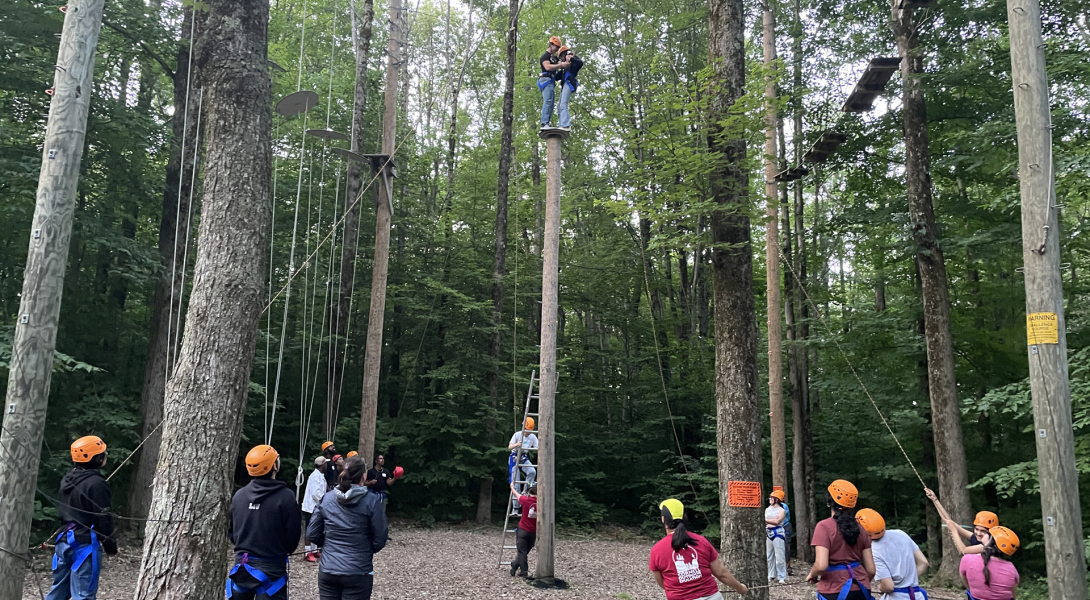 Students belay each other as they climb up a ropes course.