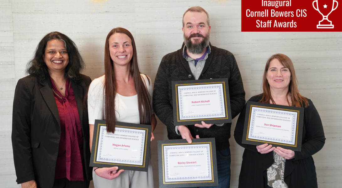 Four people stand against a wall holding plaques.