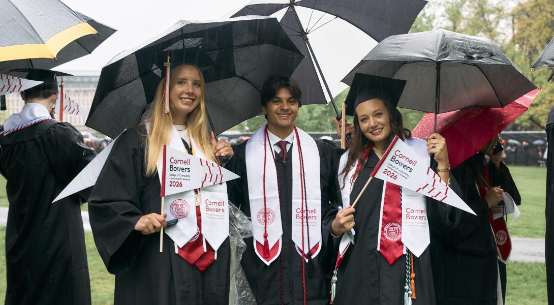 Three students pose under umbrellas 
