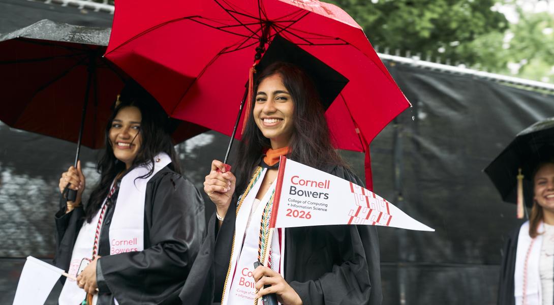 two female graduastes with long dark hair and tan skin wave white Bowers pennants 