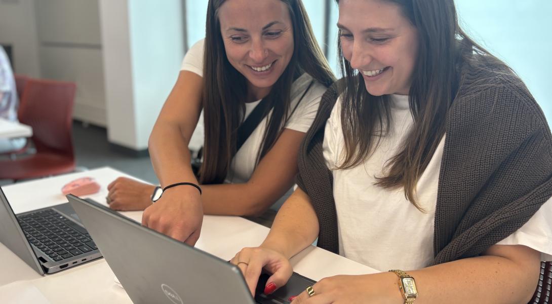 Two females with long brown hair work on a laptop together