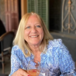 A color photo of Claudia Wojcinski sitting at an outdoor patio with a drink