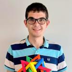A photo of Matthew Eichhorn, a man with short dark brown hair, glasses, and a striped blue shirt, holding a colorful puzzle, in front of a gray background