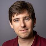 A headshot of Curran Muhlberger, a man with short brown hair and a red shirt