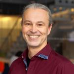 A portrait of Thorsten Joachims, a man with gray hair and a dark red shirt smiling at the camera