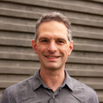 A photo of Stephen Marschner, a smiling man with short gray hair and a gray shirt, in front of a gray background