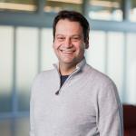 a man with short brown hair wearing a gray sweater