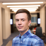 A color photo of a man smiling for a photo in a hallway.