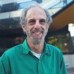 man in green shirt smiling in front of Gates Hall