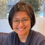 Color photo of woman with chin length black hair, round wire framed glasses