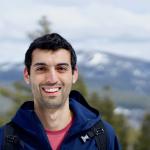 color portrait of man with dark hair on mountain, smiling
