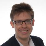 A photo of Immanuel Trummer, a man with short brown hair, glasses,and a white shirt with a black jacket in front of a white background