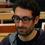 man with glasses, short dark hair and beard looking down
