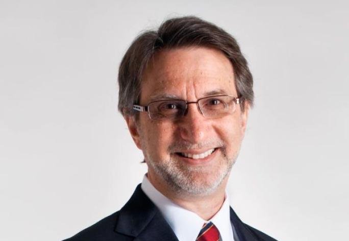 A photo of Haym Hirsh, a smiling man with brown hair and glasses in a navy suit and red tie, in front of a gray background