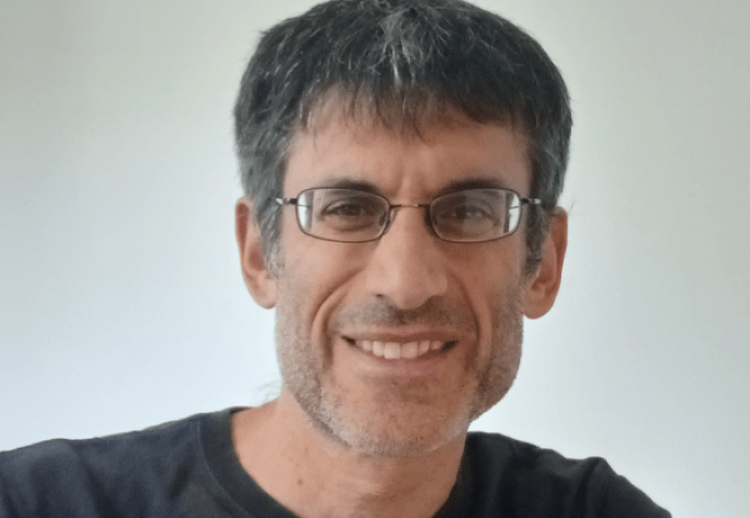 A photo of Robert Kleinberg, a smiling man with short gray hair, glasses and a black shirt in front of a gray background