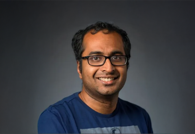 A photo of Bharath Hariharan, a smiling man with short dark hair, glasses and a blue shirt in front of a gray background