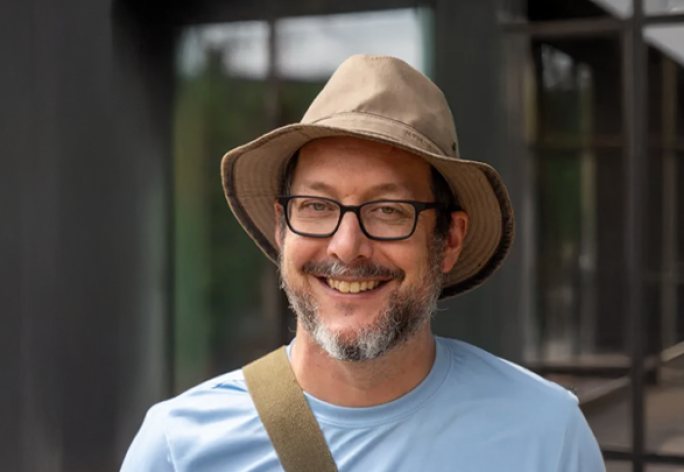 A photo of David Bindel, a man in glasses, a brown hat and blue tshirt