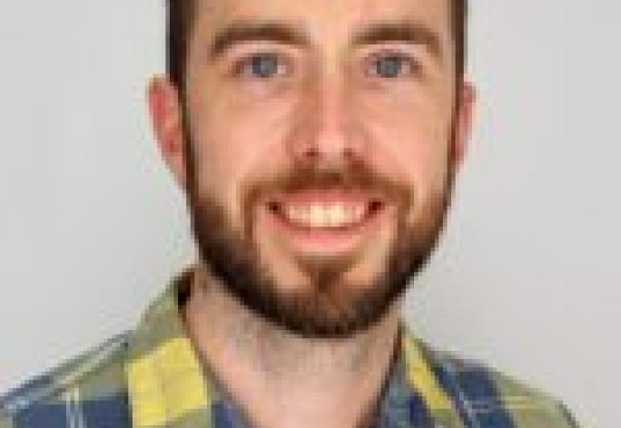 a man with short brown hair and a beard wearing a yellow and blue plaid shirt